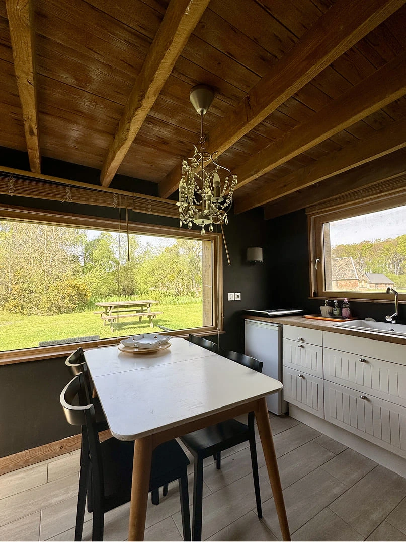 Cuisine lumineuse et salle à manger dans un gîte du Domaine de la Ferme de Fourges, avec vue sur le jardin verdoyant et mobilier en bois, typique d’un séjour en Normandie.